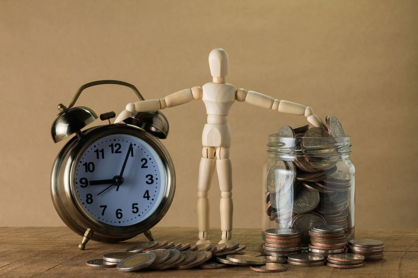 An alarm clock and a wooden figure standing beside a jar full of coins