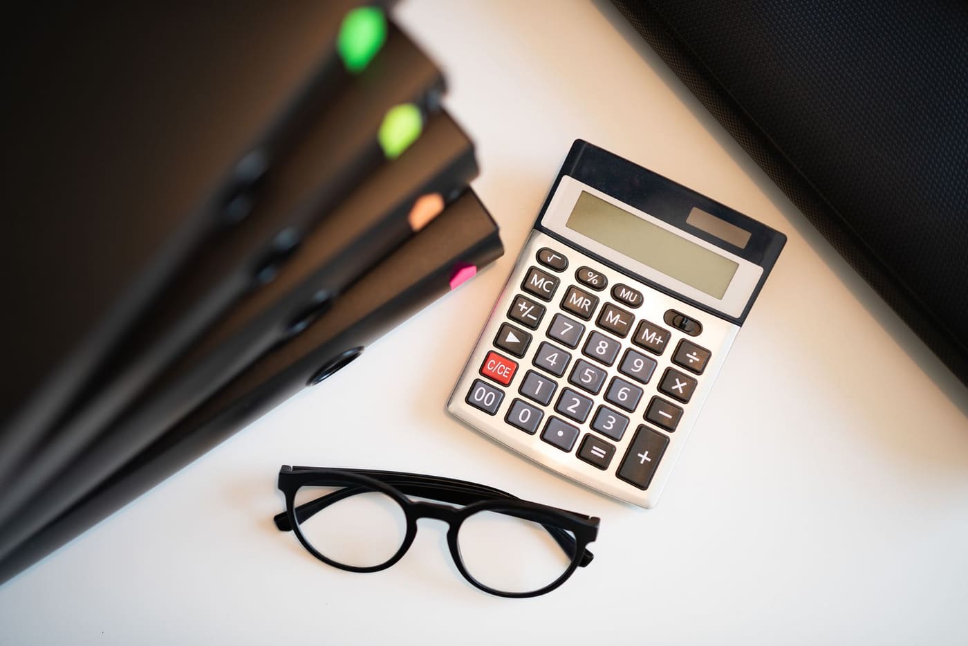 A desk calculator, black-framed glasses and a stack of folders seen from above