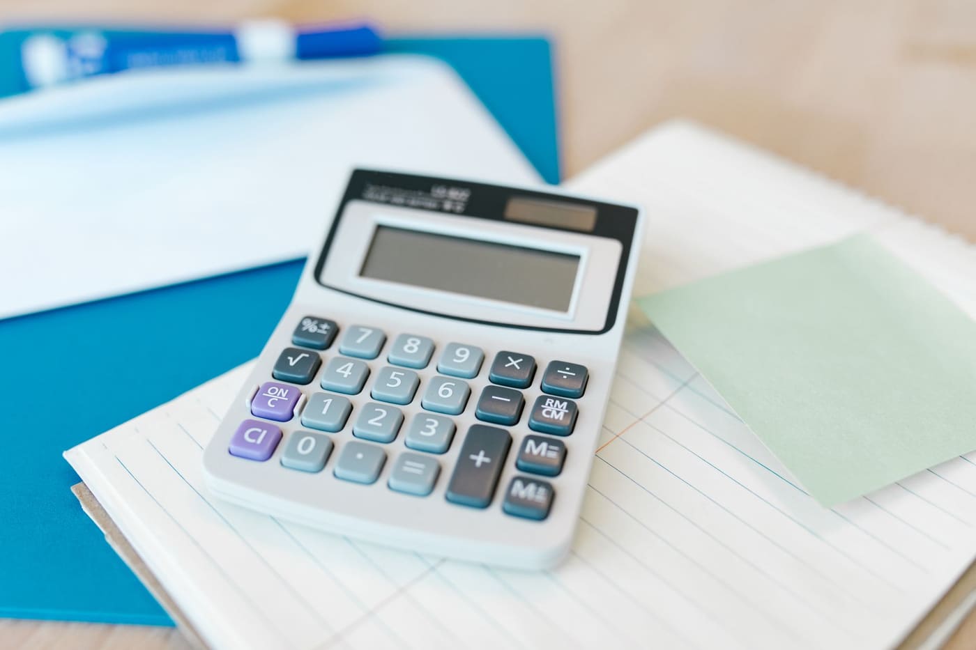 A white desk calculator resting on lined paper beside a blue folder