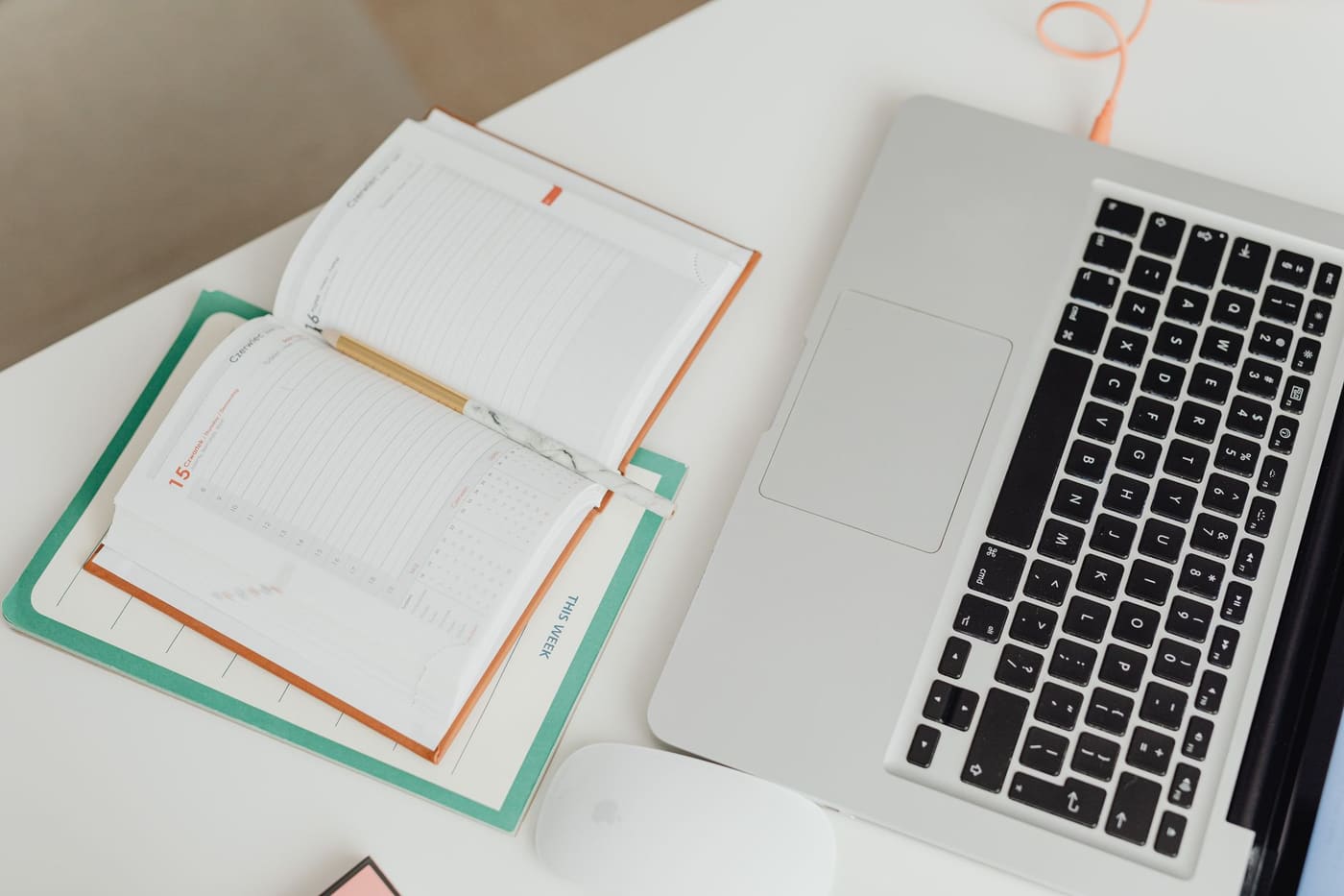 A laptop and an open notebook on a clean desk seen from above