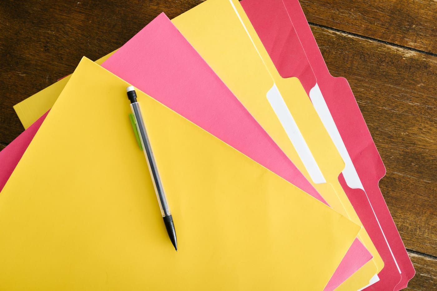 Yellow and pink file folders with a pen on a wooden table
