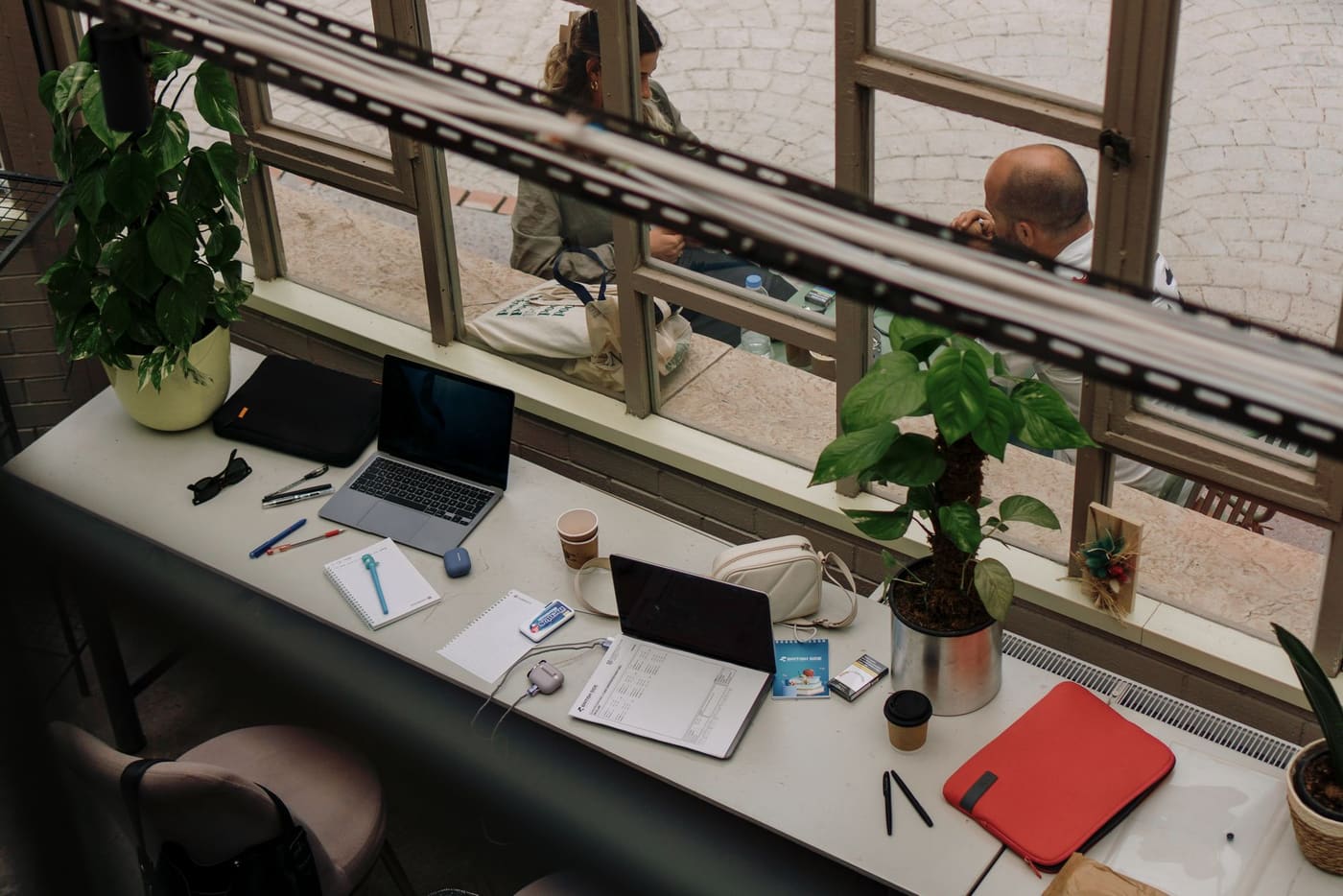 A bright desk by a window with a laptop, notebook and houseplants
