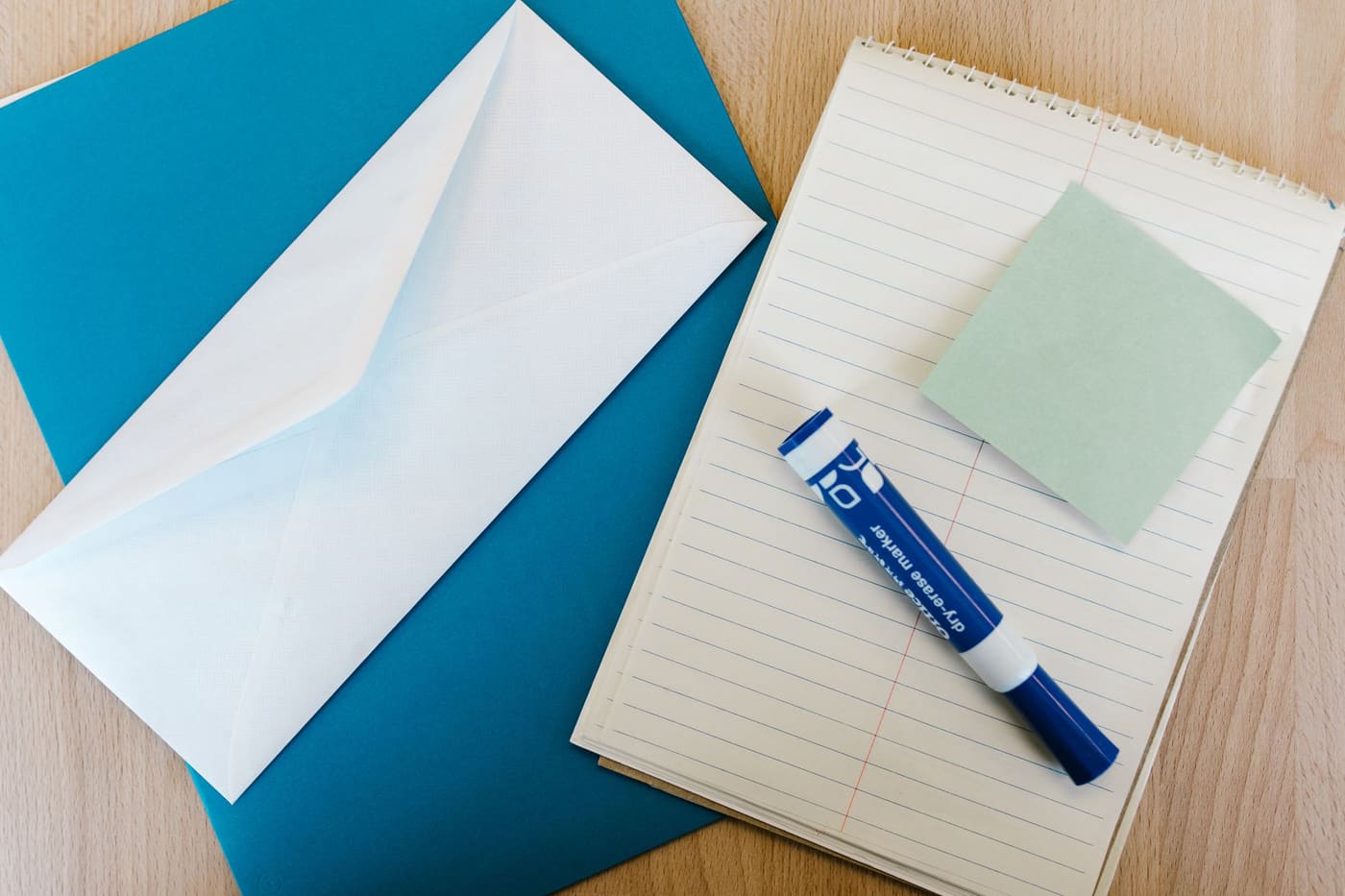 A notepad, an envelope and a marker on a wooden desk