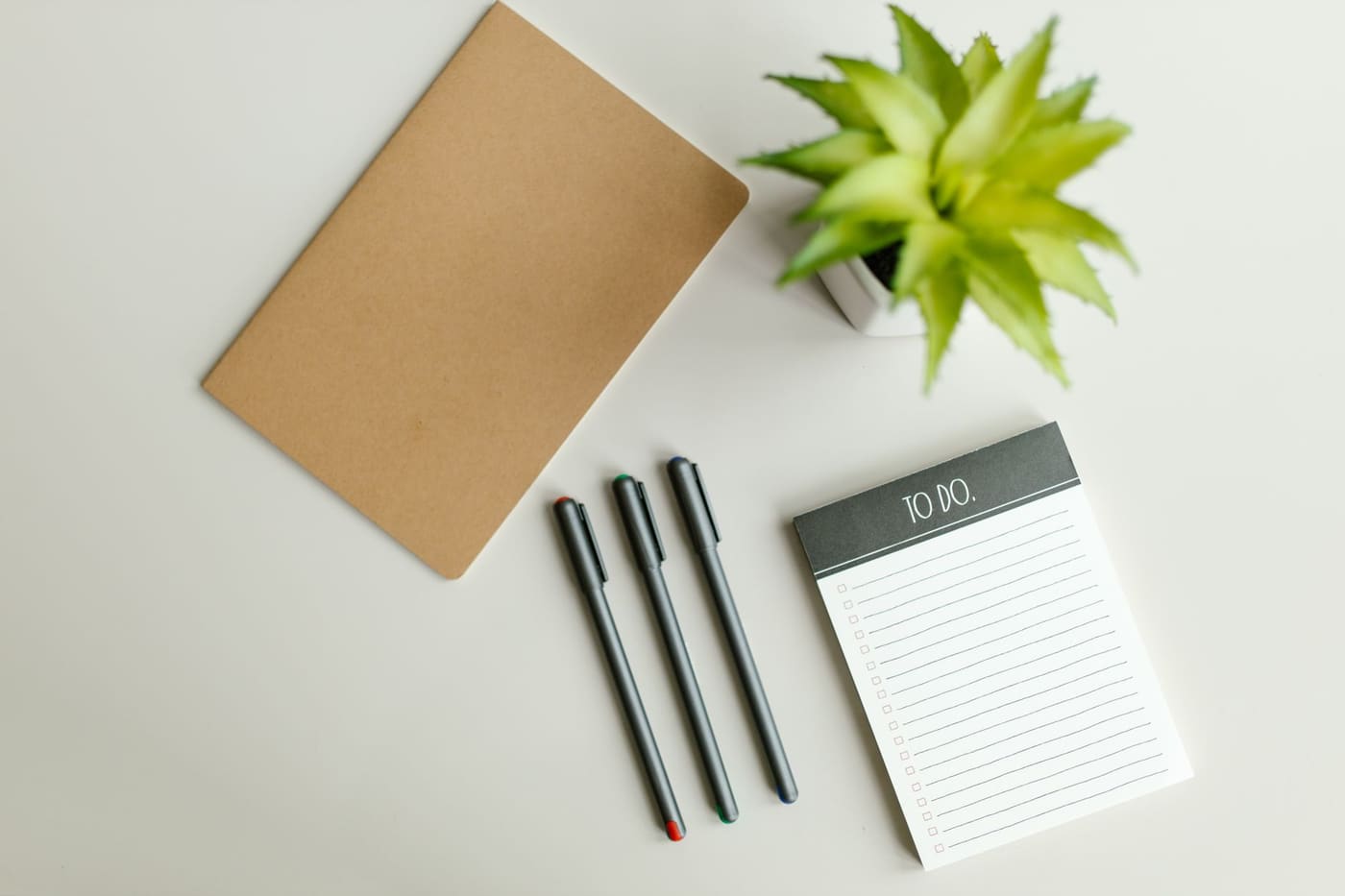 A kraft notebook, pens and a to-do pad beside a small succulent on a light desk