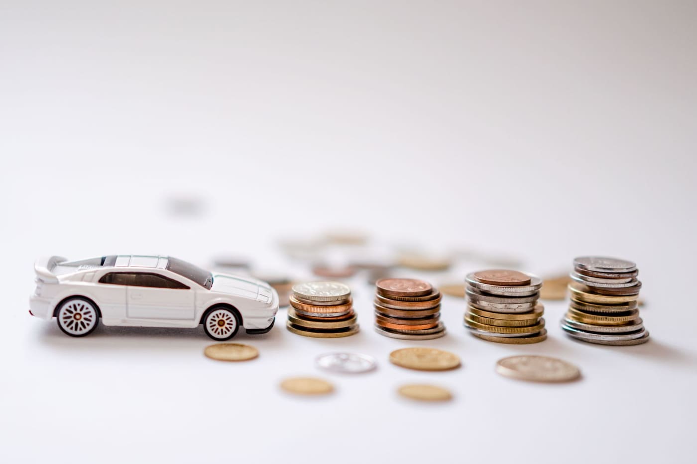 A small white toy car beside several neat stacks of coins on a white surface