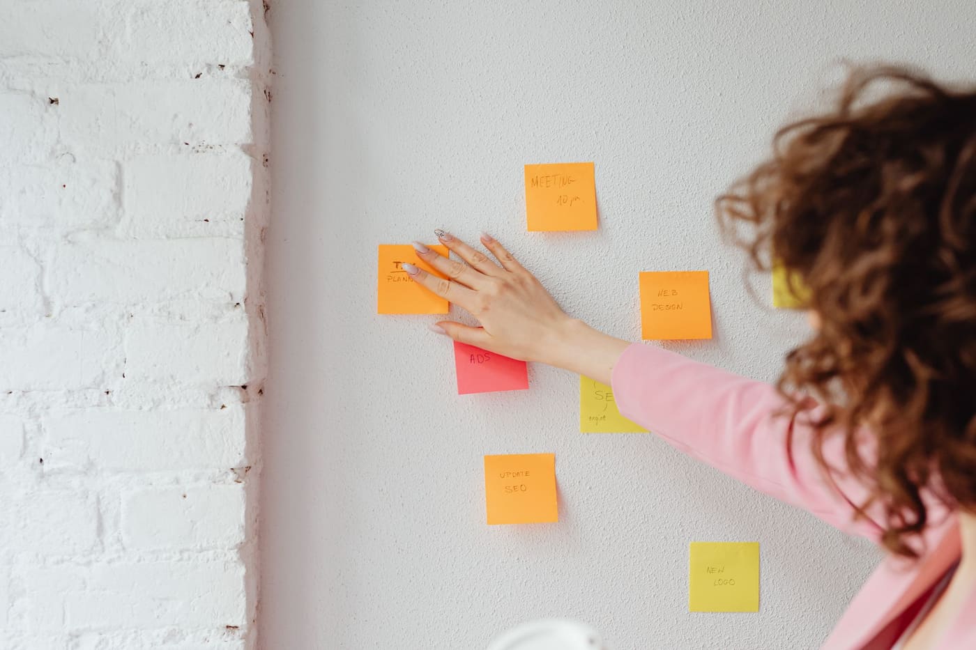 A woman placing sticky notes on a white brick wall