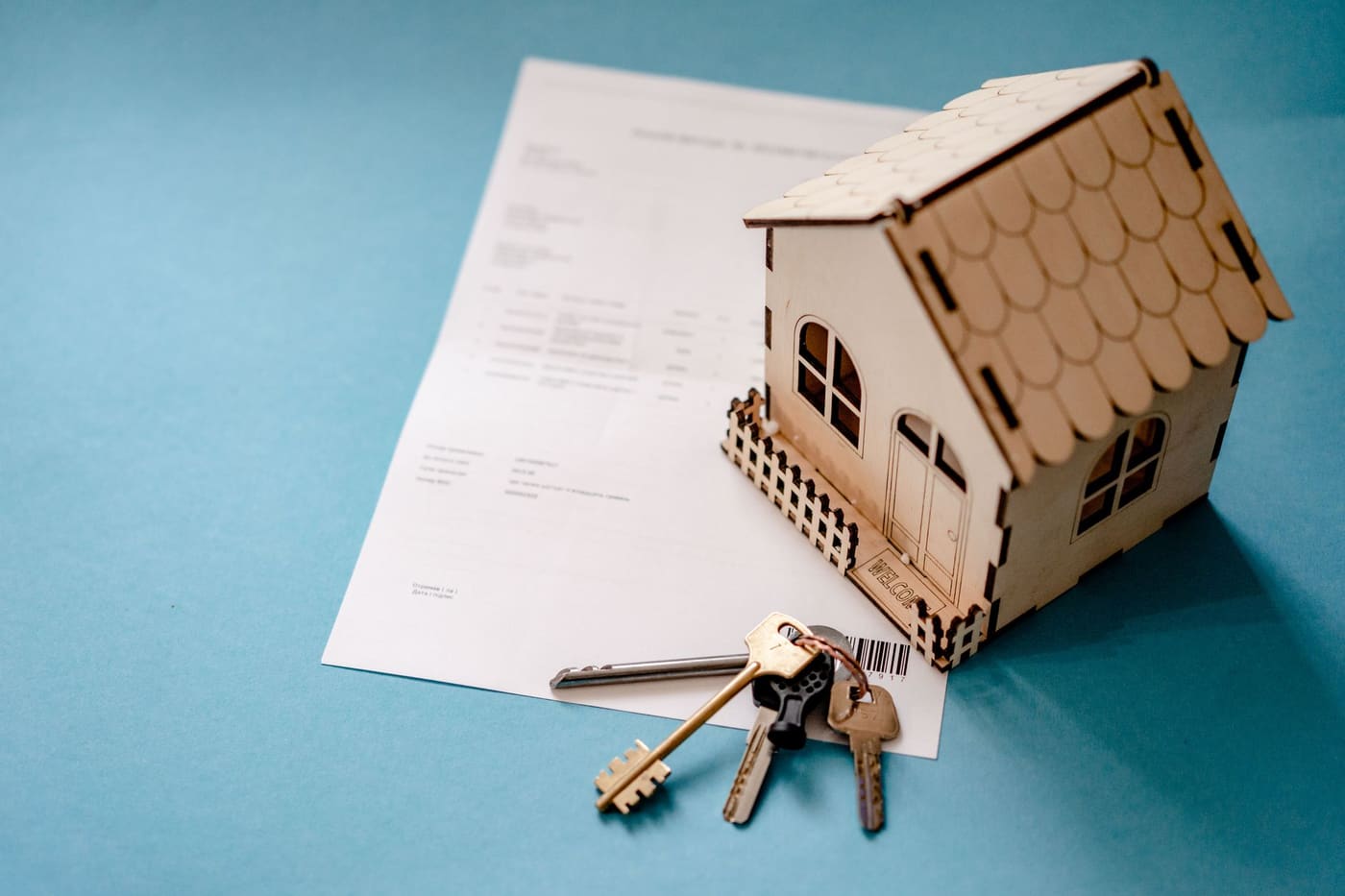 A small wooden house model with keys beside a printed contract on a blue surface